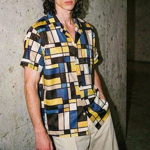 Peut inclure: Chemise à manches courtes avec un motif géométrique jaune, bleu, noir et blanc. La chemise a un col classique et est associée à un pantalon beige. Le motif de la chemise présente une disposition en grille de formes rectangulaires.