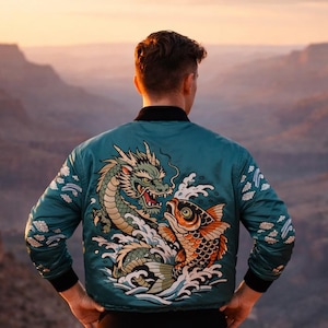 Könnte beinhalten: Türkisfarbene Bomberjacke mit einem gestickten Drachen- und Koi-Fisch-Design. Die Jacke hat schwarze gerippte Bündchen und einen schwarzen Kragen. Die Person trägt eine blaue Jeans.