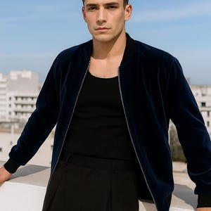 May include: A navy blue bomber jacket with a black shirt and black pants. The jacket has a zipper closure and ribbed cuffs. The outfit is worn by a person standing outside with a blue sky background.