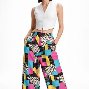 Könnte beinhalten: Eine ärmellose weiße Weste kombiniert mit einer weiten Hose. Die Hose hat ein lebendiges geometrisches Muster mit rosa, blauen, gelben und schwarzen Formen und einem Dalmatiner-ähnlichen Druck.