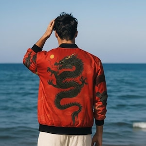 May include: Red bomber jacket featuring a black dragon design on the back. The jacket has black trim on the collar, cuffs, and hem. The dragon is black with gold detailing. The background is a blue sea and sky.