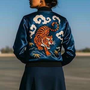 May include: A navy blue satin bomber jacket with a tiger design on the back. The tiger is orange and black, surrounded by white clouds. The jacket has a black collar and cuffs. The model is wearing a navy blue skirt.