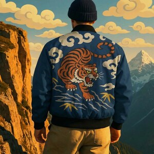 May include: A blue bomber jacket with a tiger design on the back. The tiger is orange and black, with white clouds and yellow accents. The jacket has a black collar and cuffs. The background shows a mountain range and a cloudy sky.