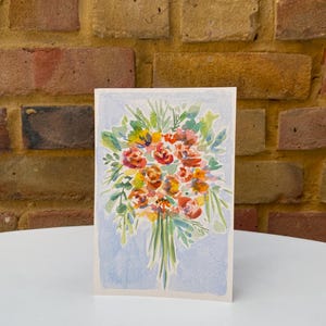 May include: A watercolor painting of a bouquet of flowers in shades of orange, red, and yellow, with green leaves. The artwork is on a rectangular card with a light blue background.