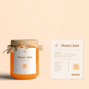 May include: A glass jar of honey jam with a brown paper lid and a white label that says "Honey Jam" and "Organic Fruit Jam". The label also has a small peach icon. The jar is sitting on a light peach background. A white card with the text "Honey Jam" and nutritional information is to the right of the jar.