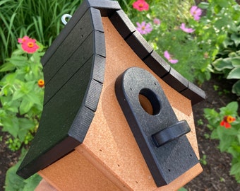 May include: A brown and black birdhouse with a rounded roof and a black entrance hole. The birdhouse has a black metal hook on the top.