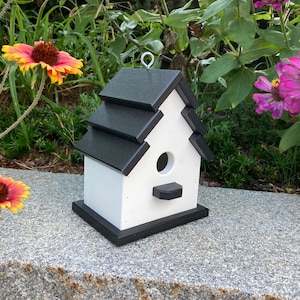 May include: A white birdhouse with a black roof and trim. The birdhouse has a small opening for birds to enter and a perch on the front.