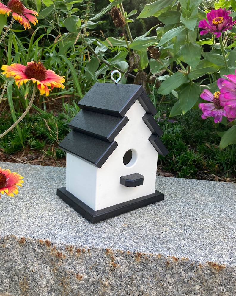 May include: A white birdhouse with a black roof and trim. The birdhouse has a small opening for birds to enter and a perch on the front.