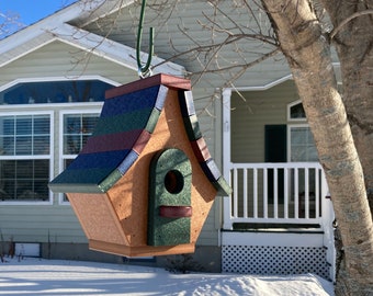 May include: A wooden birdhouse with a green, blue, and red roof. The birdhouse is hanging from a tree branch and has a small opening for birds to enter.