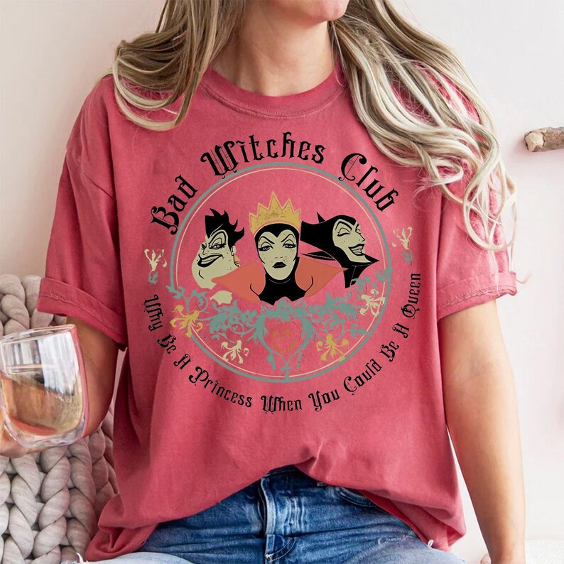 Peut inclure: T-shirt rouge avec un motif circulaire repr&eacute;sentant trois personnages de sorci&egrave;res de dessins anim&eacute;s et le texte "Bad Witches Club". Le motif comprend la phrase "Why Be A Princess When You Could Be A Queen."