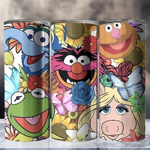 May include: Three stainless steel tumblers featuring Muppet characters Gonzo, Animal, and Miss Piggy. The tumblers are decorated with colourful floral and butterfly designs, with a white background.
