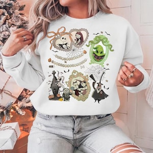 May include: White sweatshirt featuring multiple framed illustrations of characters from "The Nightmare Before Christmas." The frames are in various shapes and colors, with images of Jack Skellington, Sally, and Oogie Boogie. The text "The Nightmare Before Christmas" is also present.