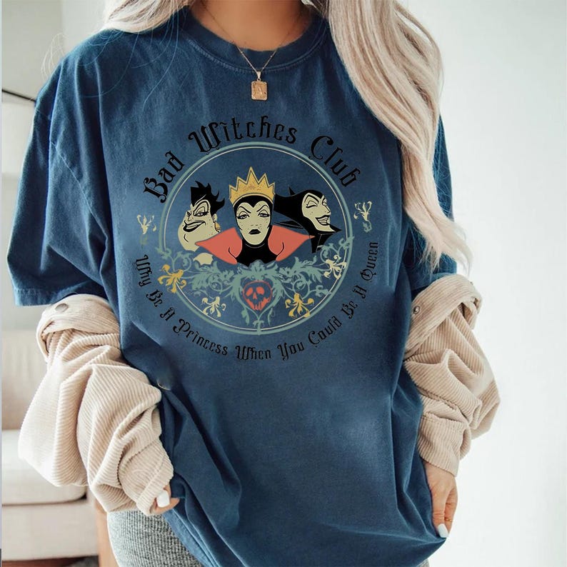 Peut inclure: T-shirt bleu marine avec un motif circulaire. Le motif comprend le texte "Bad Witches Club" et "Why Be A Princess When You Could Be A Queen", ainsi que des illustrations de trois sorci&egrave;res de dessins anim&eacute;s.