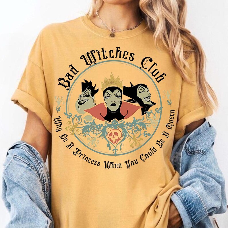 Peut inclure: T-shirt jaune moutarde avec un motif circulaire. Le motif comprend le texte "Bad Witches Club" et "Why Be A Princess When You Could Be A Queen", ainsi que des illustrations de trois sorci&egrave;res de dessins anim&eacute;s.
