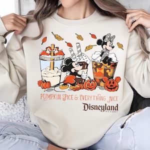 May include: Beige sweatshirt with a graphic featuring Mickey and Minnie Mouse, Chip and Dale, and pumpkin spice drinks. The text reads "Pumpkin Spice & Everything Nice" and "Disneyland Resort."