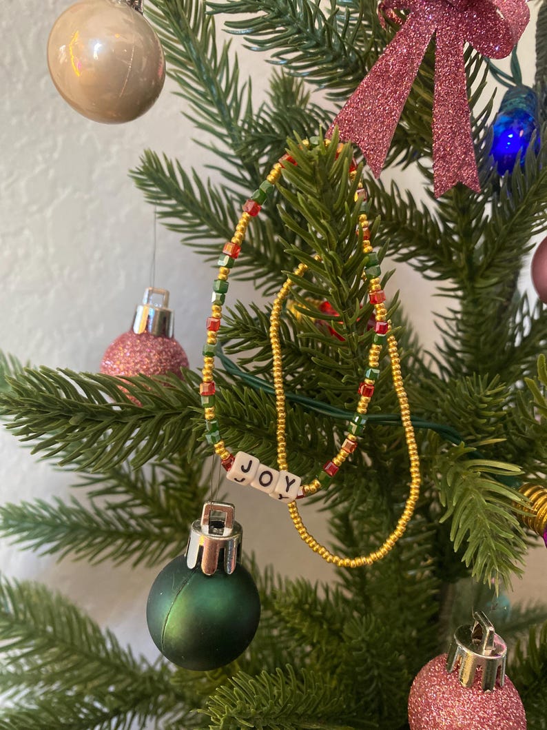 Pode incluir: Um enfeite de &aacute;rvore de Natal com um colar de contas e a palavra "JOY" escrita em contas brancas.