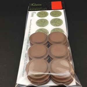 May include: A package of miniature accessories. The package contains several brown, circular bases and a sheet of green decals. The text on the package reads "SHYGROUND ACCESSORIES FOR MINIATURES" and "Round Decals for HG 32mm Bases - Green".