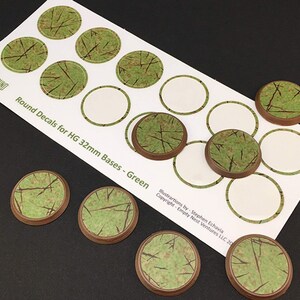 May include: A sheet of round green decals for 32mm bases, with a green and brown textured design. The sheet has the text "Round Decals for HG 32mm Bases - Green" and the "SHIGROUND" logo. Several individual decals are also visible.