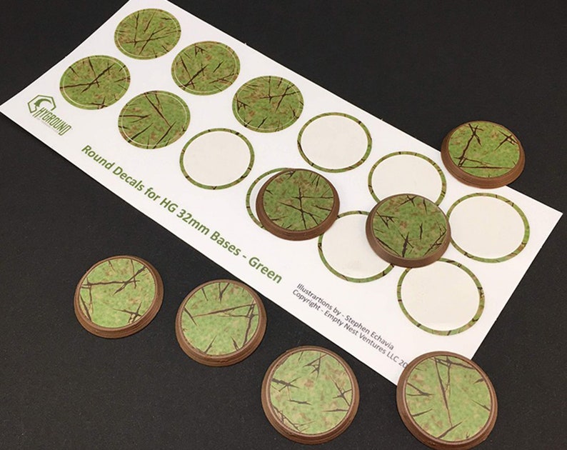 May include: A sheet of round green decals for 32mm bases, with a green and brown textured design. The sheet has the text "Round Decals for HG 32mm Bases - Green" and the "SHIGROUND" logo. Several individual decals are also visible.