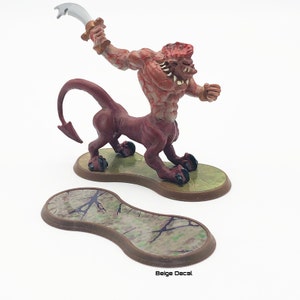 May include: A red and brown miniature figurine of a creature with a human torso and a lion's body holding a silver sword. The figurine is standing on a brown base with a green and brown pattern.