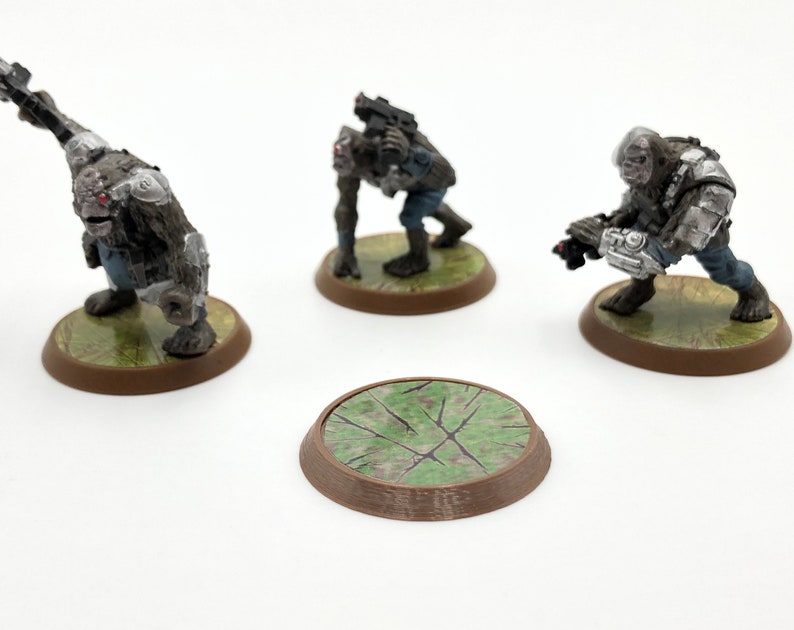 May include: Miniature figurines of fantasy creatures, each posed with weapons and armor. The figures are painted in shades of gray, brown, and blue, mounted on circular bases with a grassy texture. One base is separate.