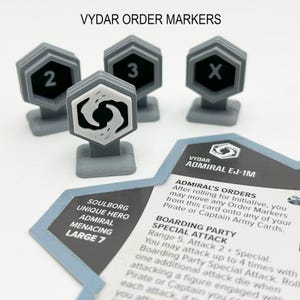 Könnte beinhalten: Vier graue Vyder Order Marker mit schwarzen Zahlen und einem weißen Symbol. Die Marker sind sechseckig mit einem kleinen Sockel. Eine Spielkarte mit Text ist ebenfalls sichtbar.