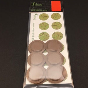 May include: A package of miniature accessories, including round decals with a green and brown design, and brown circular bases. The package is labeled "SHYGROUND ACCESSORIES FOR MINIATURES" and "Round Decals for HG 32mm."