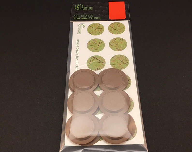 May include: A package of miniature accessories, including round decals with a green and brown design, and brown circular bases. The package is labeled "SHYGROUND ACCESSORIES FOR MINIATURES" and "Round Decals for HG 32mm."