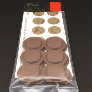 May include: A package of miniature accessories. The package contains brown round bases and oval decals with a textured, tan and brown pattern. The packaging includes the text "ACCESSORIES FOR MINIATURES".