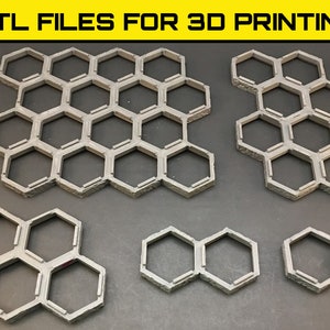 Może przedstawiać: Zestaw sześciu szarych, sześciokątnych płytek wydrukowanych w 3D. Płytki są przeznaczone do użytku w grach planszowych lub jako elementy dekoracyjne. Płytki są ułożone w różnych konfiguracjach, w tym duży wzór plastra miodu, mniejszy wzór plastra miodu i pojedynczy rząd trzech płytek.