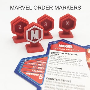 Könnte beinhalten: Rote Plastik-Ordnungsmarker mit den Zahlen 2, 3 und X sowie ein Marker mit dem Buchstaben M. Die Marker werden für ein Brettspiel verwendet. Eine Karte für das Spiel ist ebenfalls abgebildet, die Captain America aus Marvel Comics zeigt. Die Karte trägt den Text "Shield Throw Special Attack" und "Tactician".
