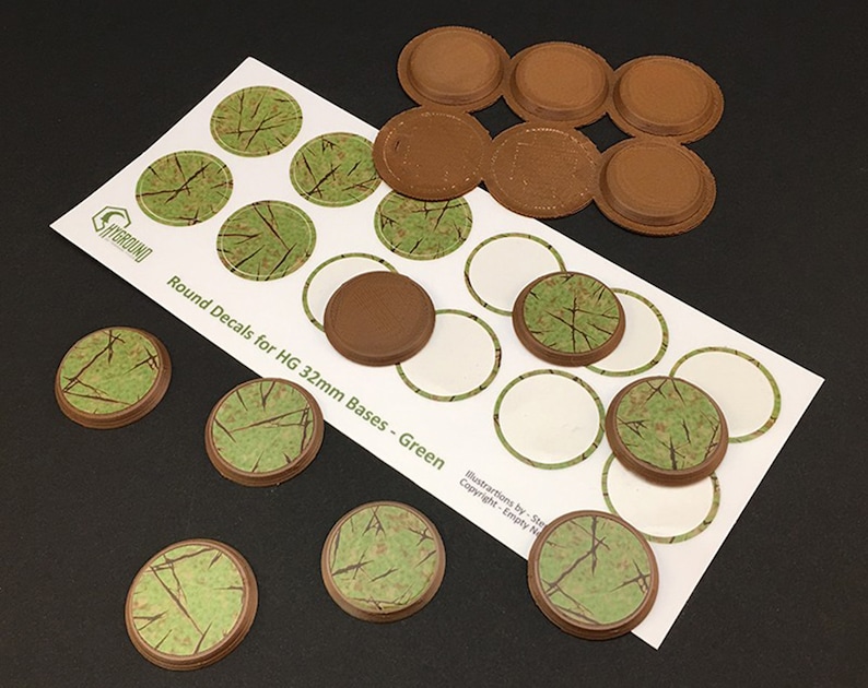 May include: A collection of round decals and bases for miniature gaming. The decals feature a green and brown grass pattern, designed for 32mm bases. The bases are a dark brown color. The text on the sheet reads "Round Decals for HG 32mm Bases - Green".
