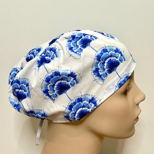 Może przedstawiać: Biały czepek chirurgiczny z powtarzającym się wzorem niebieskich kwiatowych wzorów. Czapka ma elastyczną opaskę zapewniającą bezpieczne dopasowanie. Tkanina jest lekkim, oddychającym materiałem.