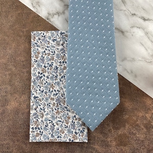 May include: A blue patterned tie and a white pocket square with a blue floral pattern.