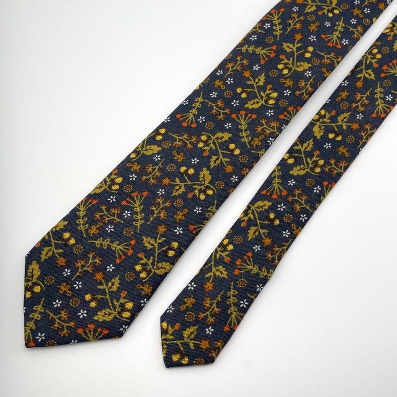 May include: A navy blue tie with a repeating floral pattern in shades of gold, orange, and white. The tie is made of a textured fabric and is displayed on a white background. The floral design includes small flowers and sprigs.