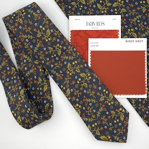 May include: A navy blue tie with a floral pattern in gold, orange, and white. The tie is next to a matching pocket square and color swatches from David's Bridal and Birdy Grey, including Sienna, Lace, and Chiffon Auburn.