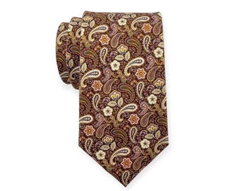 May include: A necktie featuring a deep brown background with a repeating pattern of intricate paisley shapes and small floral motifs in shades of cream, gold, orange, and dark purple. The tie is folded at the top, showing the fabric texture.