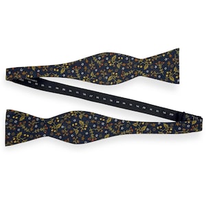 May include: A navy blue adjustable bow tie with a floral pattern in gold, orange, and white. The bow tie is open, showing the adjustable strap with size markings from 14.5 to 20 inches.