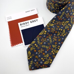 May include: A navy blue tie with a floral pattern in yellow, orange, and white. Two color swatches are visible, one auburn and the other mesh navy, with the text "Birdy Grey" on the labels.