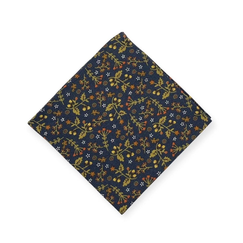May include: A navy blue pocket square with a repeating floral pattern in gold, orange, and white. The square is folded in a diamond shape, showcasing the detailed botanical design. This accessory is suitable for formal or casual wear.