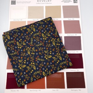 May include: A navy blue fabric swatch with a floral pattern in gold, orange, and white, displayed over a color chart. The chart includes various shades of pink, brown, and burgundy, with color names like "Rose Quartz" and "Cabernet".