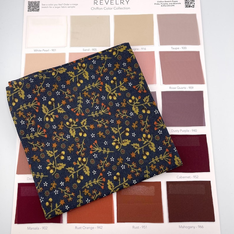 May include: A navy blue fabric swatch with a floral pattern in gold, orange, and white, displayed over a color chart. The chart includes various shades of pink, brown, and burgundy, with color names like "Rose Quartz" and "Cabernet".