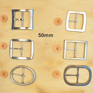 Peut inclure: Une collection de six boucles de ceinture en métal argenté de formes variées, incluant des designs carrés, rectangulaires et ovales. Chaque boucle est étiquetée avec un petit jeton circulaire numéroté de un à six. Le texte 50mm est centré.