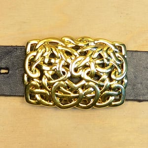 May include: A gold-colored belt buckle with an intricate Celtic knot design.