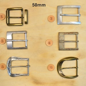 May include: Six belt buckles labeled 1 through 6, each measuring 50mm. The collection includes various metallic finishes: antique brass, polished silver, brushed steel, weathered iron, and smooth gold-tone, featuring both rectangular and curved shapes.