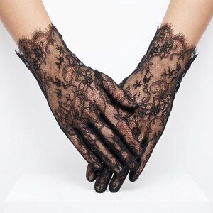 May include: Black lace gloves with intricate floral patterns. The gloves have a delicate, scalloped edge at the wrist. The sheer fabric allows the skin to be visible, creating an elegant and romantic look.