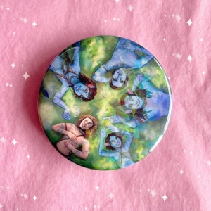 May include: A round button featuring a watercolour painting of five blue-skinned individuals with long, flowing hair. The individuals are surrounded by green foliage and are looking at each other. The button is ideal for fans of Avatar.