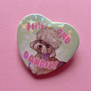 Puede incluir: Un botón en forma de corazón con un fondo verde y una ilustración de dibujos animados de un perro marrón y blanco con el texto "Fine and Dandie!" en letras rosas.