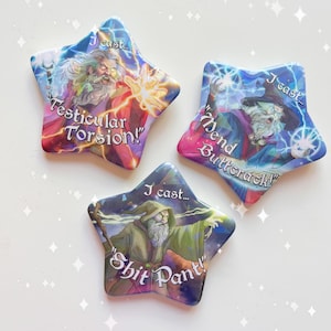 Op de afbeelding: Drie stervormige knoppen met kleurrijke illustraties van tovenaars die spreuken uitspreken. De tekst op de knoppen luidt "I cast... Testicular Torsion!" "I cast... Mend Buttcrack!" en "I cast... Shit Pant!"