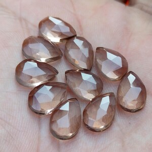 Pu&ograve; includere: Una collezione di dieci perle di pietra preziosa sfaccettate a forma di lacrima di colore marrone chiaro. Le perle sono traslucide e hanno una finitura liscia e lucida.